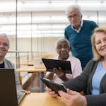 Elderly group using digital tablets and laptops in a study session indoors.